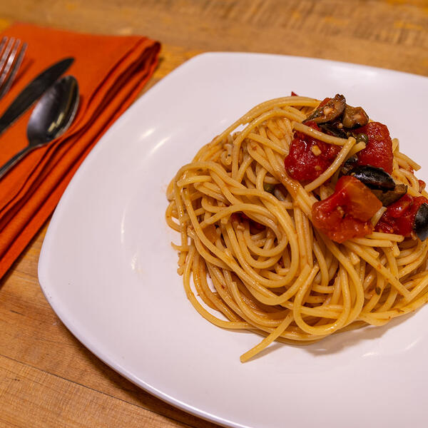 A dish of pasta puttanesca next to eating utensils on a napkin.