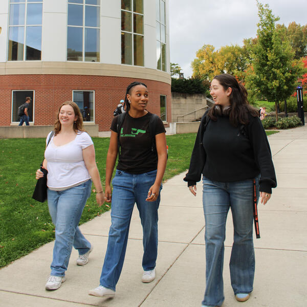 Three students are chatting and walking near library  